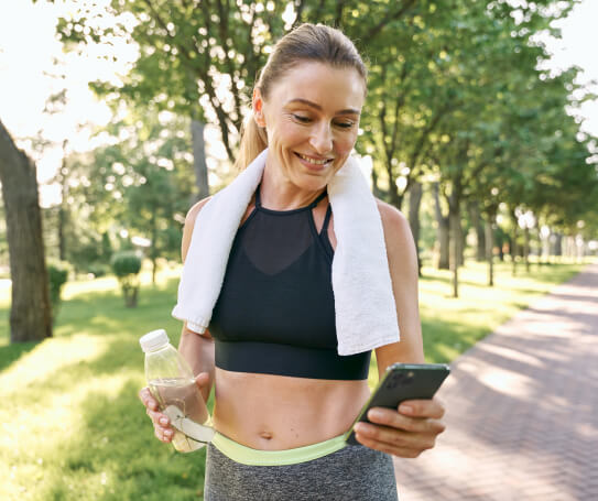 A woman holding a towel around her neck looking at a phone at an iv drip bar.