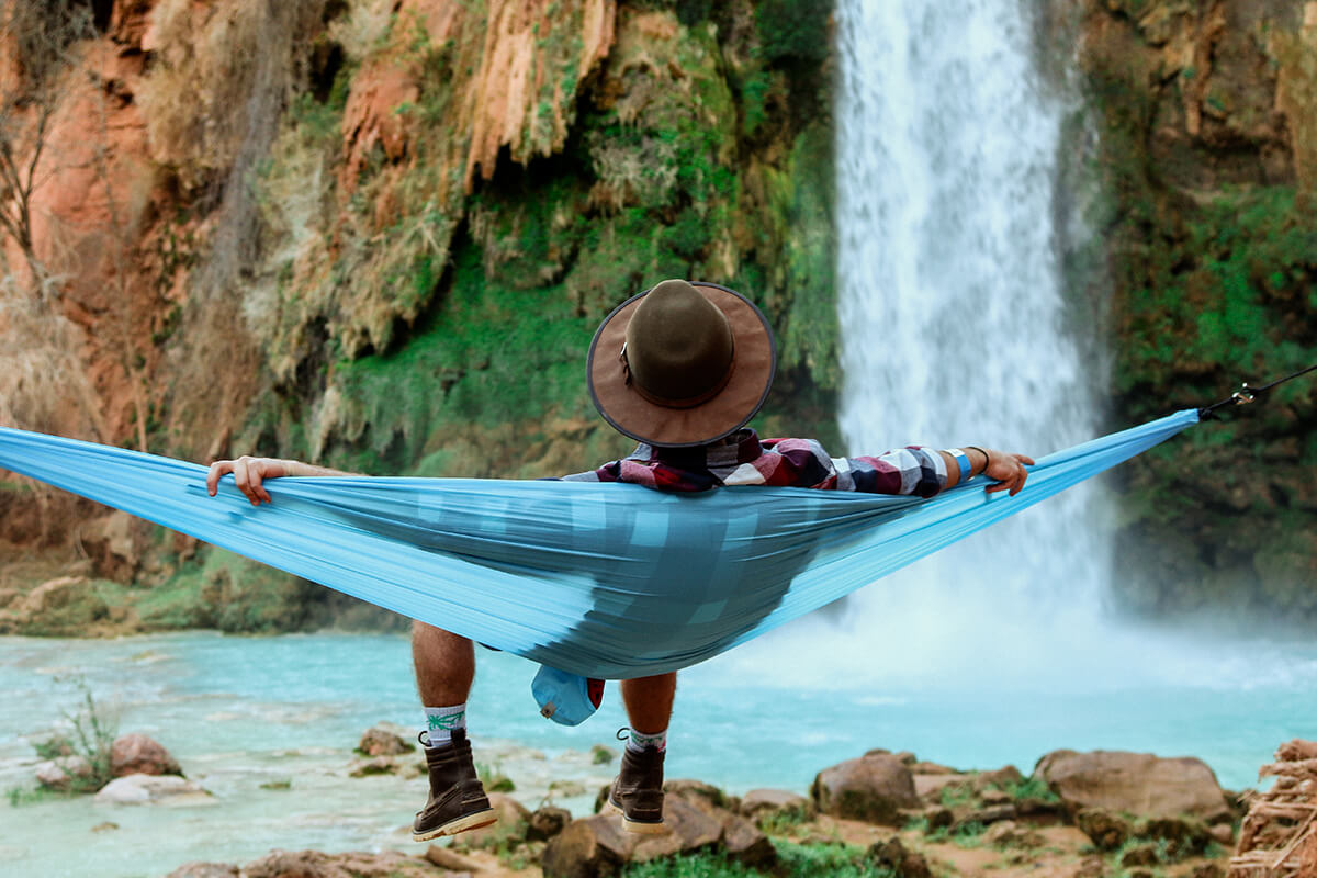 A man receiving IV therapy in a hammock near a waterfall.